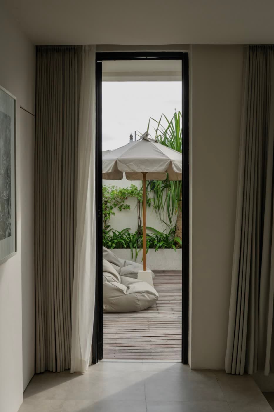 A villa bedroom door open onto a garden terrace with a sun umbrella and a bean bag